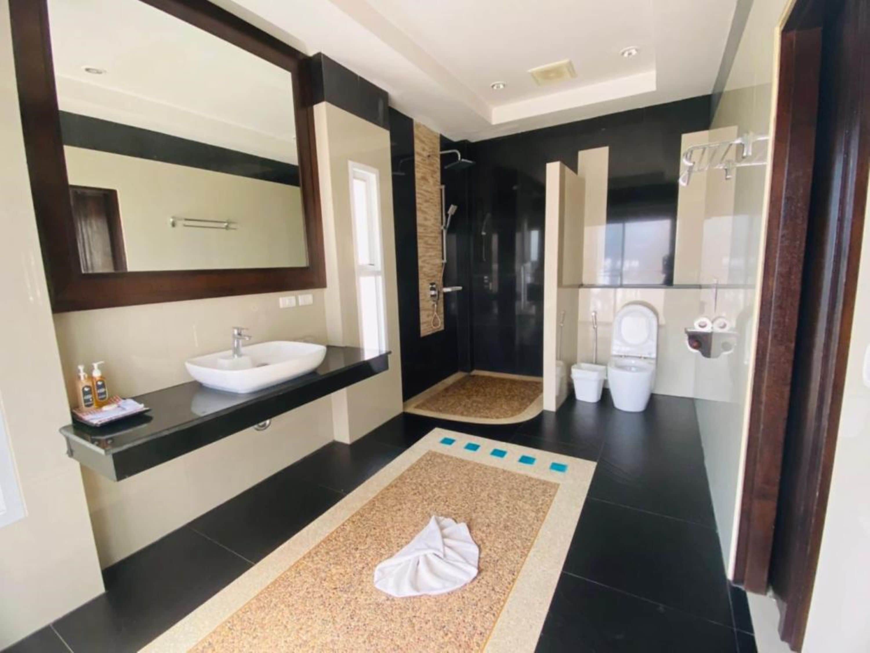 Un baño moderno con un espejo grande, un lavamanos blanco, una ducha y dos inodoros.