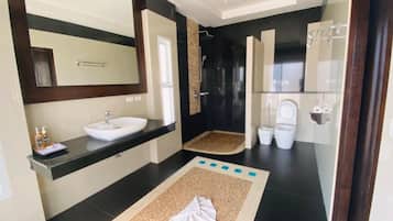 Un baño moderno con un espejo grande, un lavamanos blanco, una ducha y dos inodoros.