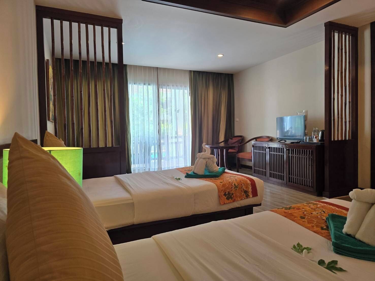 Habitación de hotel con dos camas, un escritorio con televisor y vistas al exterior a través de amplias ventanas.