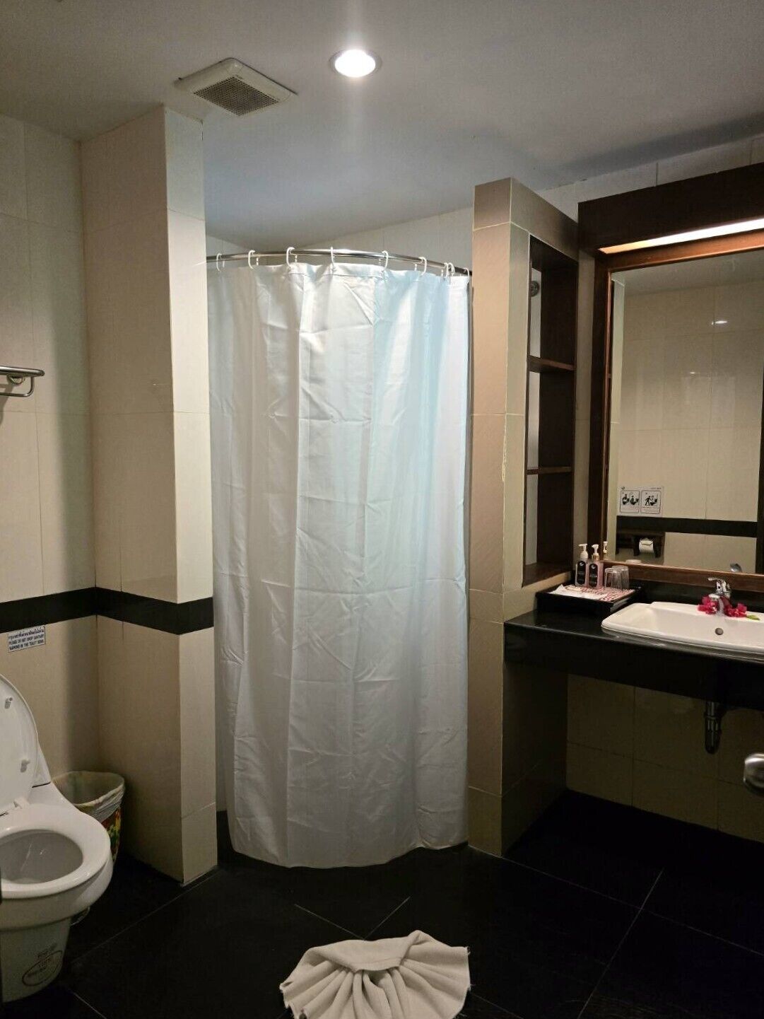 A bathroom with a white shower curtain, a toilet, a sink with toiletries, and a mirror.