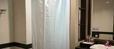 A bathroom with a white shower curtain, a toilet, a sink with toiletries, and a mirror.