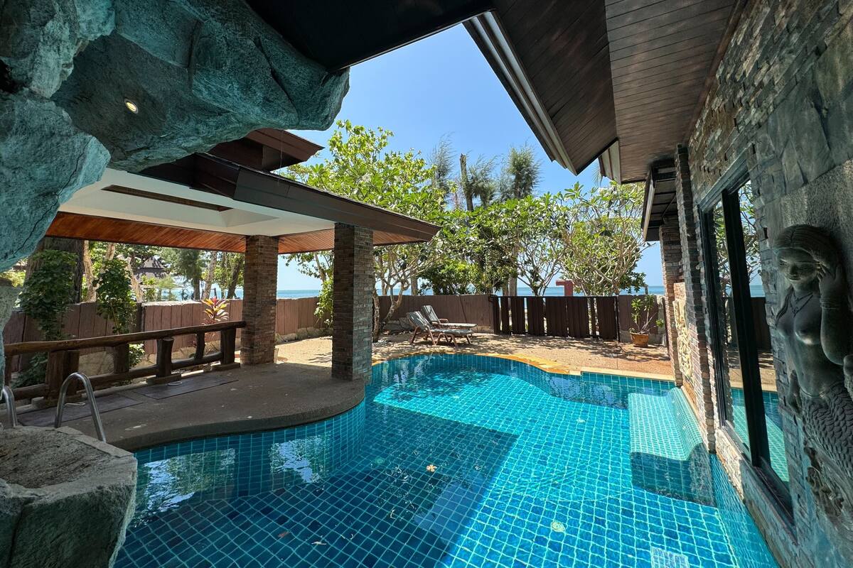 Un espace piscine agrémenté d’un mur en pierre, d’une terrasse en bois et offrant une vue sur l’océan.