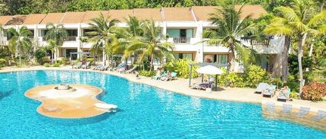 A resort with a large swimming pool, palm trees, and a hillside backdrop.