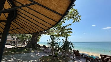 Ett område vid stranden med ett avskärmat sittområde, solstolar och utsikt över havet.