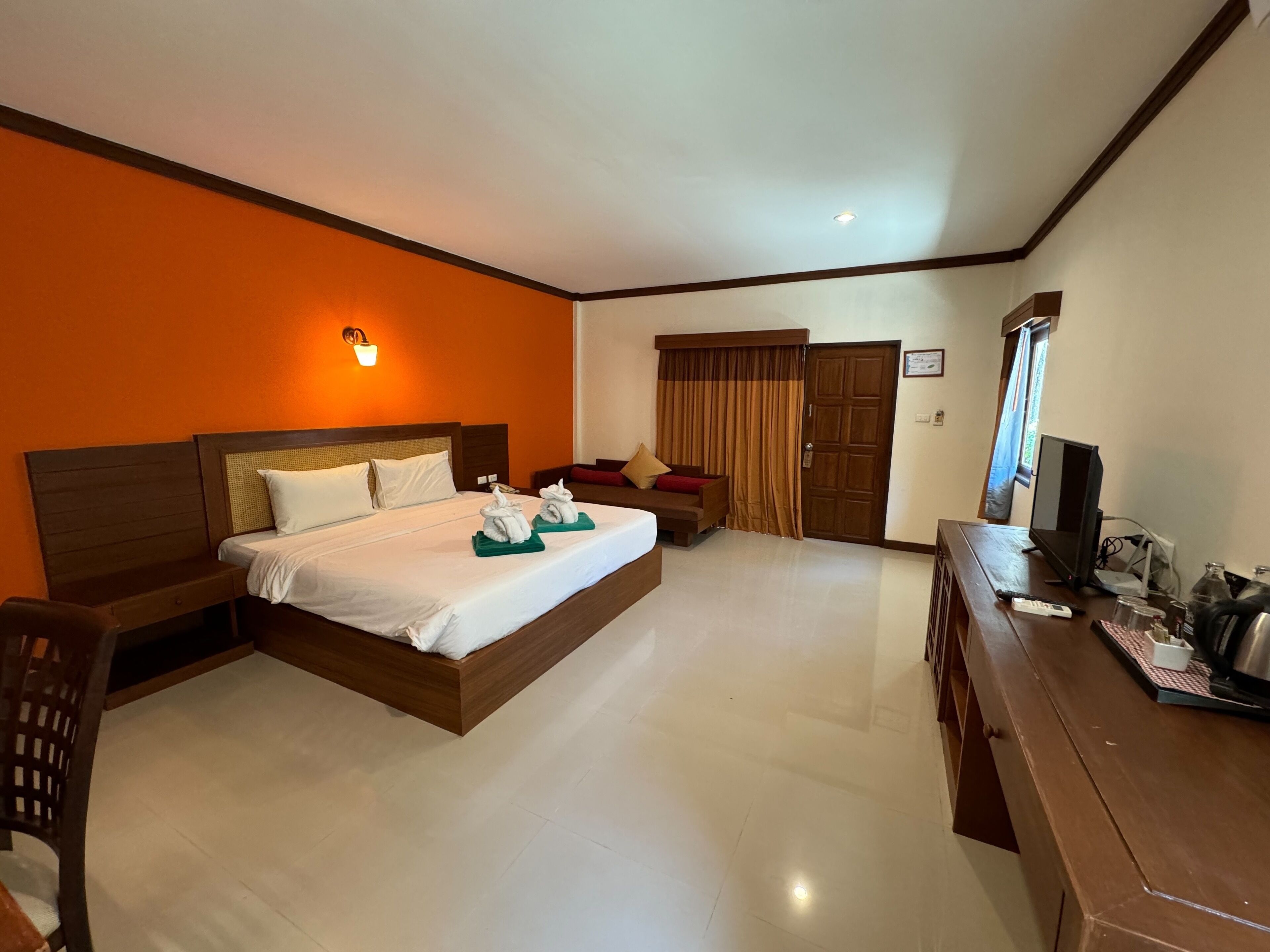 A hotel room with a bed, a desk with a TV, and a window.