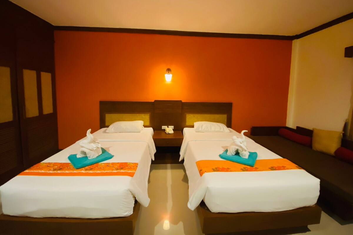 Une chambre d’hôtel avec deux lits simples, une table de chevet avec un téléphone et une lampe fixée au mur.