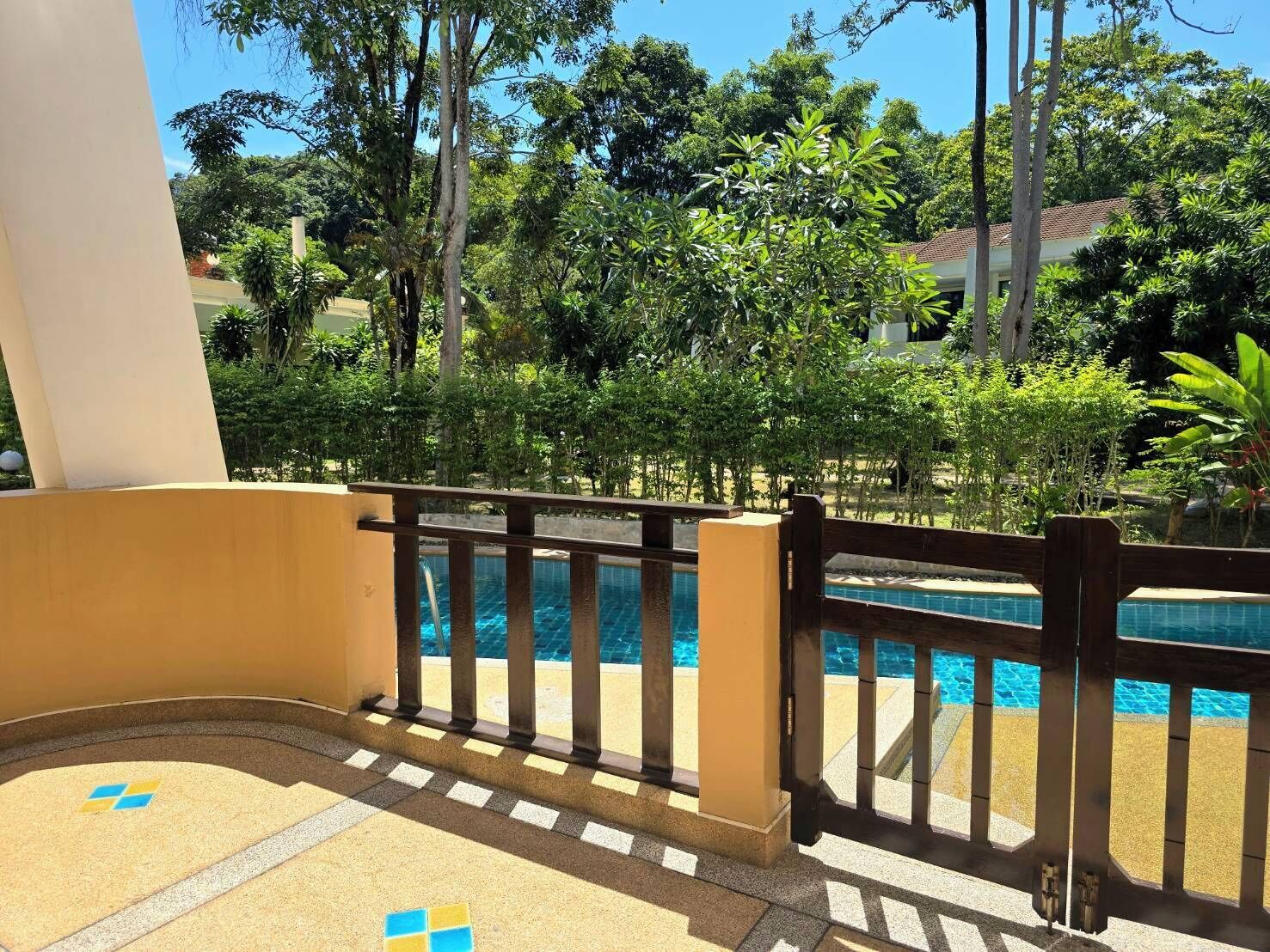 A pool area with a wooden fence, surrounded by lush greenery and a clear blue sky.