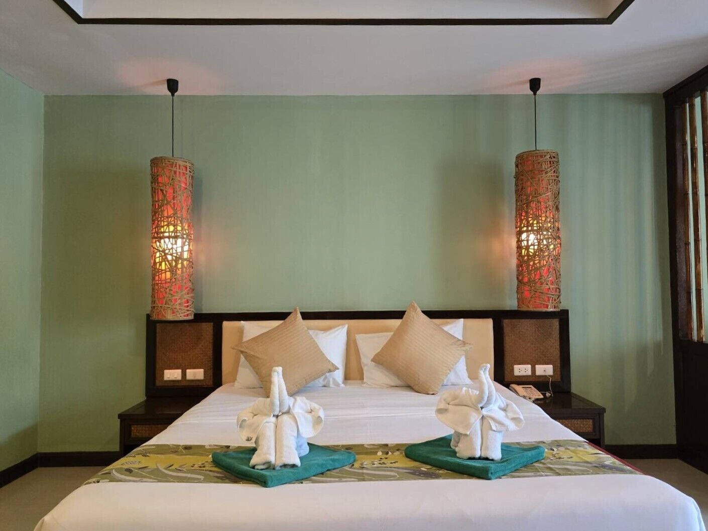 Habitación de hotel con una cama grande, dos mesitas de noche, dos lámparas de pared y dos toallas dispuestas sobre la cama.