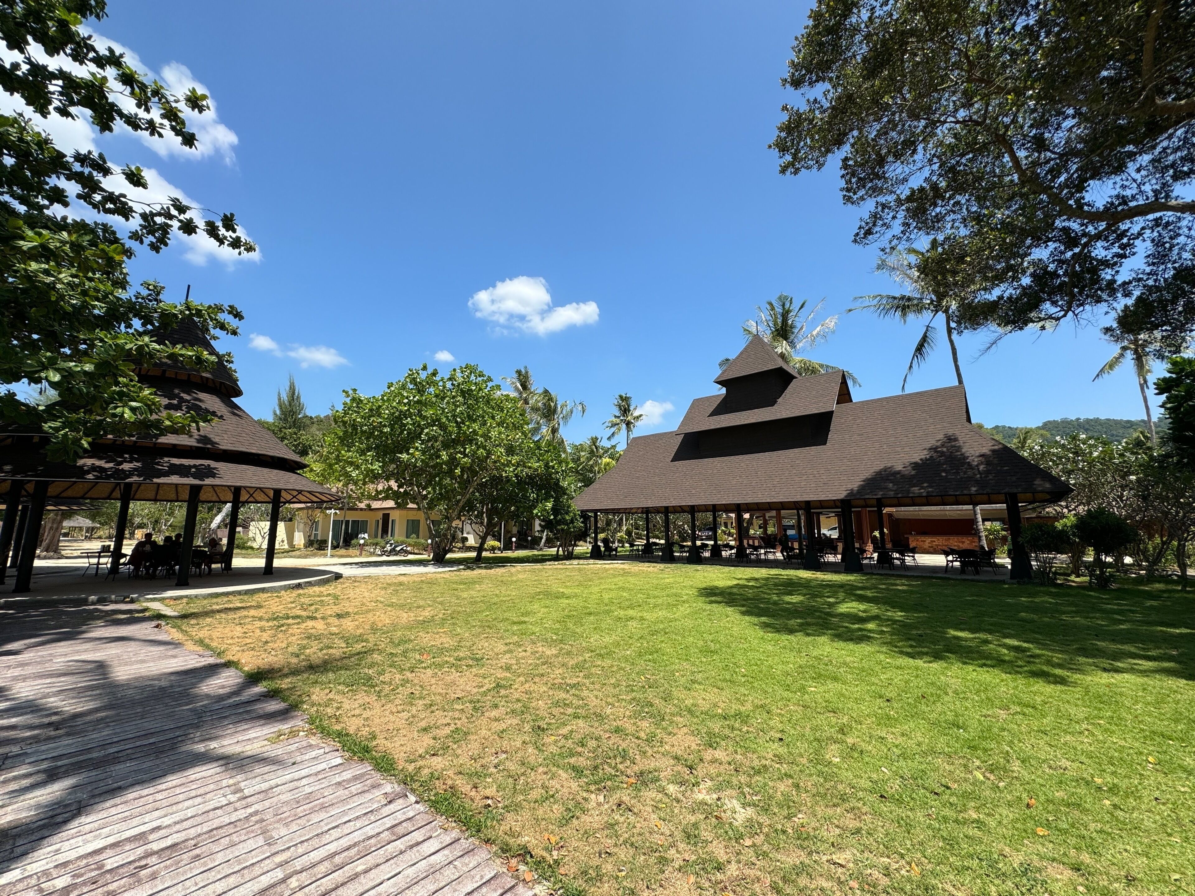 A resort with multiple thatched-roof pavilions, a grassy lawn, and a clear blue sky.