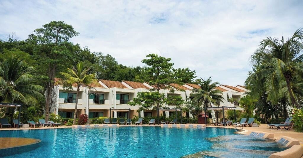 Ein Hotel mit Swimmingpool, umgeben von Palmen und Liegestühlen.