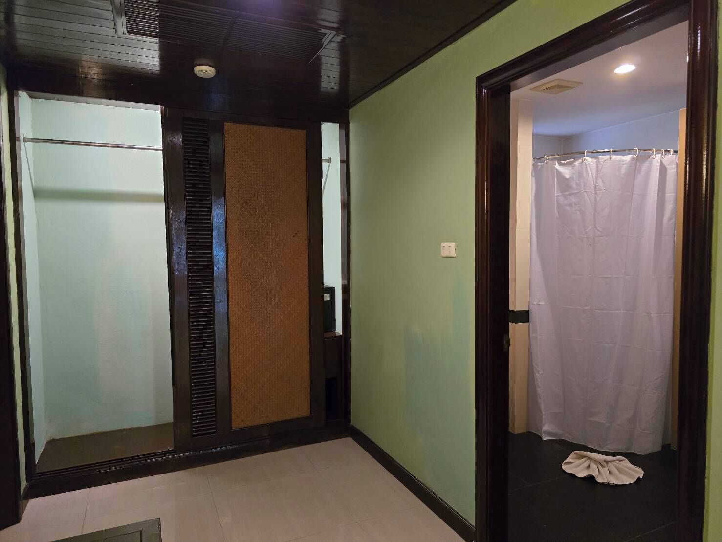 A hallway with a glass door, a wooden panel, and a white curtain in a bathroom.