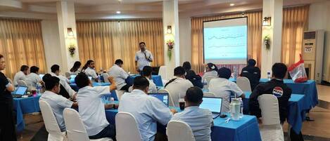A conference room with round tables, attendees seated, and a presenter at the front.