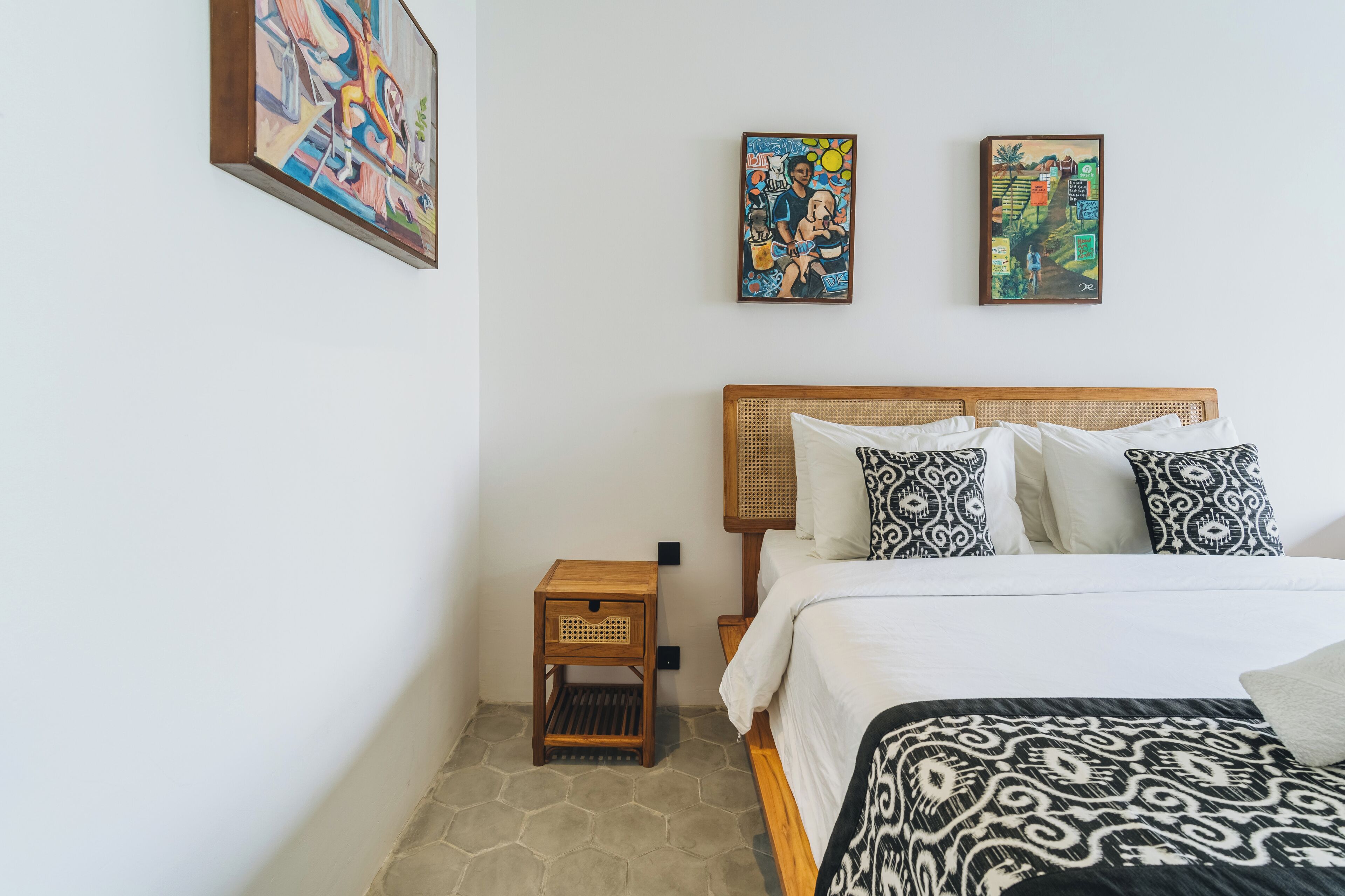 Une chambre à coucher avec un lit en bois, des coussins à motifs et deux œuvres d’art accrochées au mur.