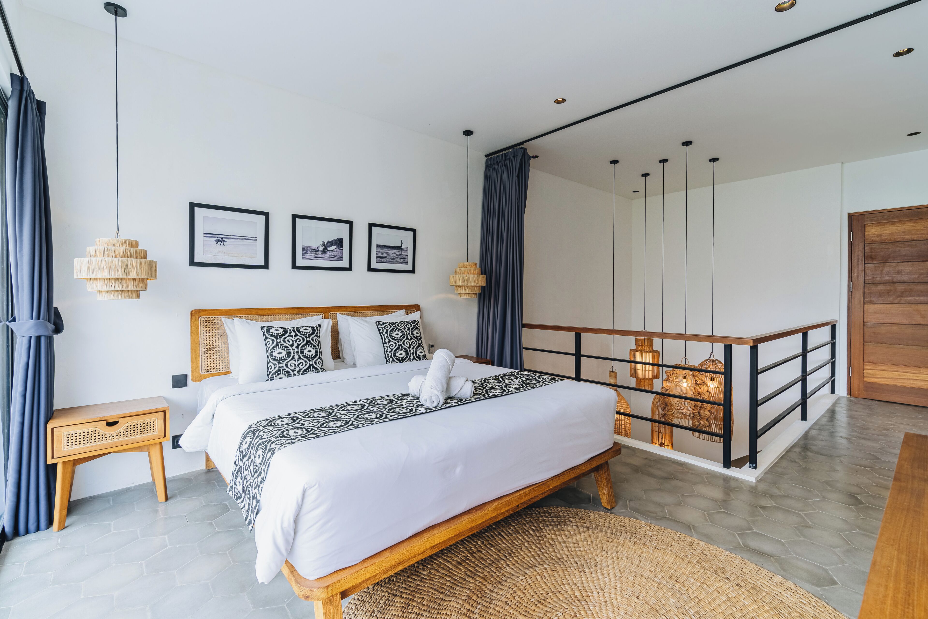 A modern bedroom with a large bed, wooden headboard, and a balcony with a railing.