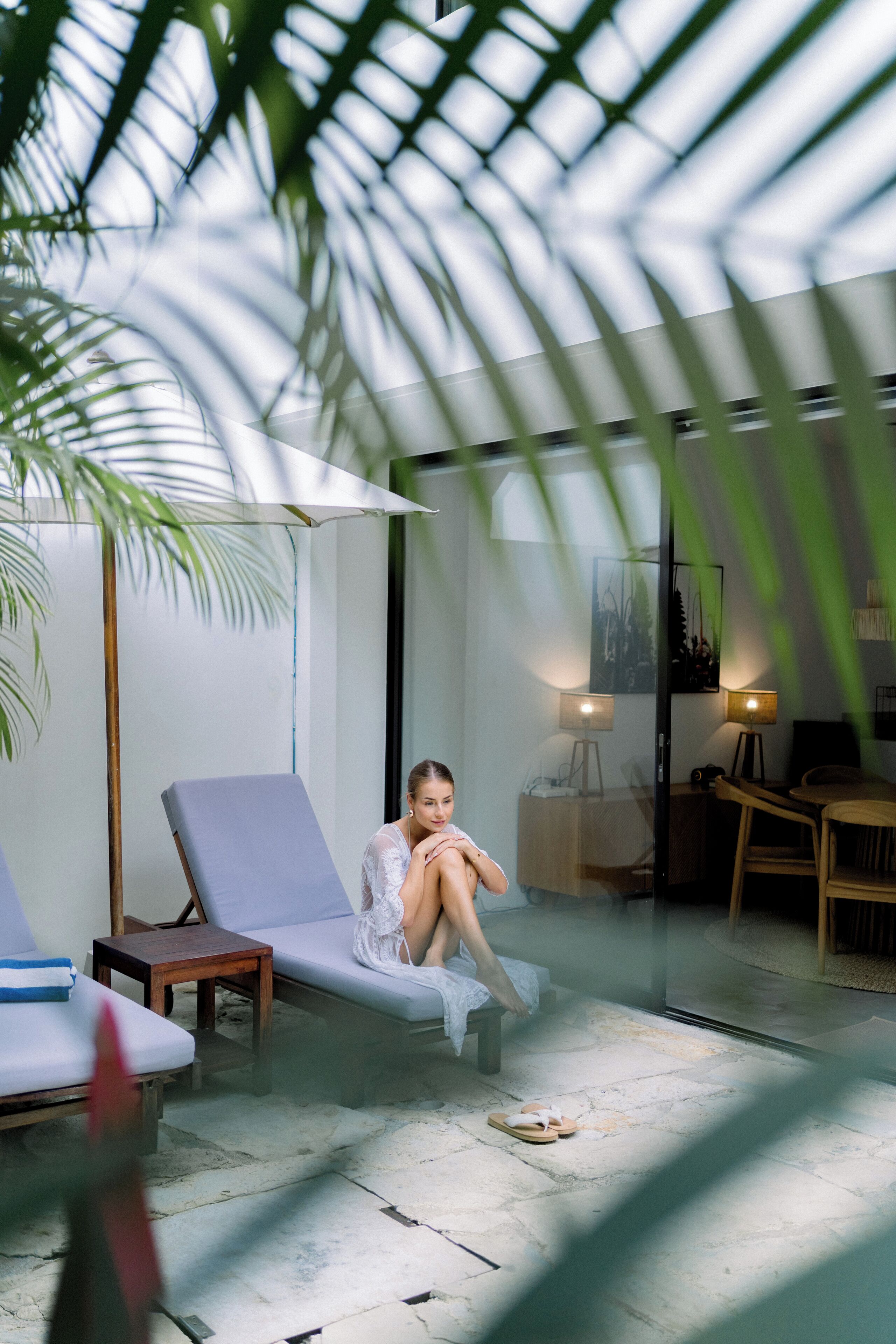 A room with a glass partition, a lounge chair, a small table, and a lamp.