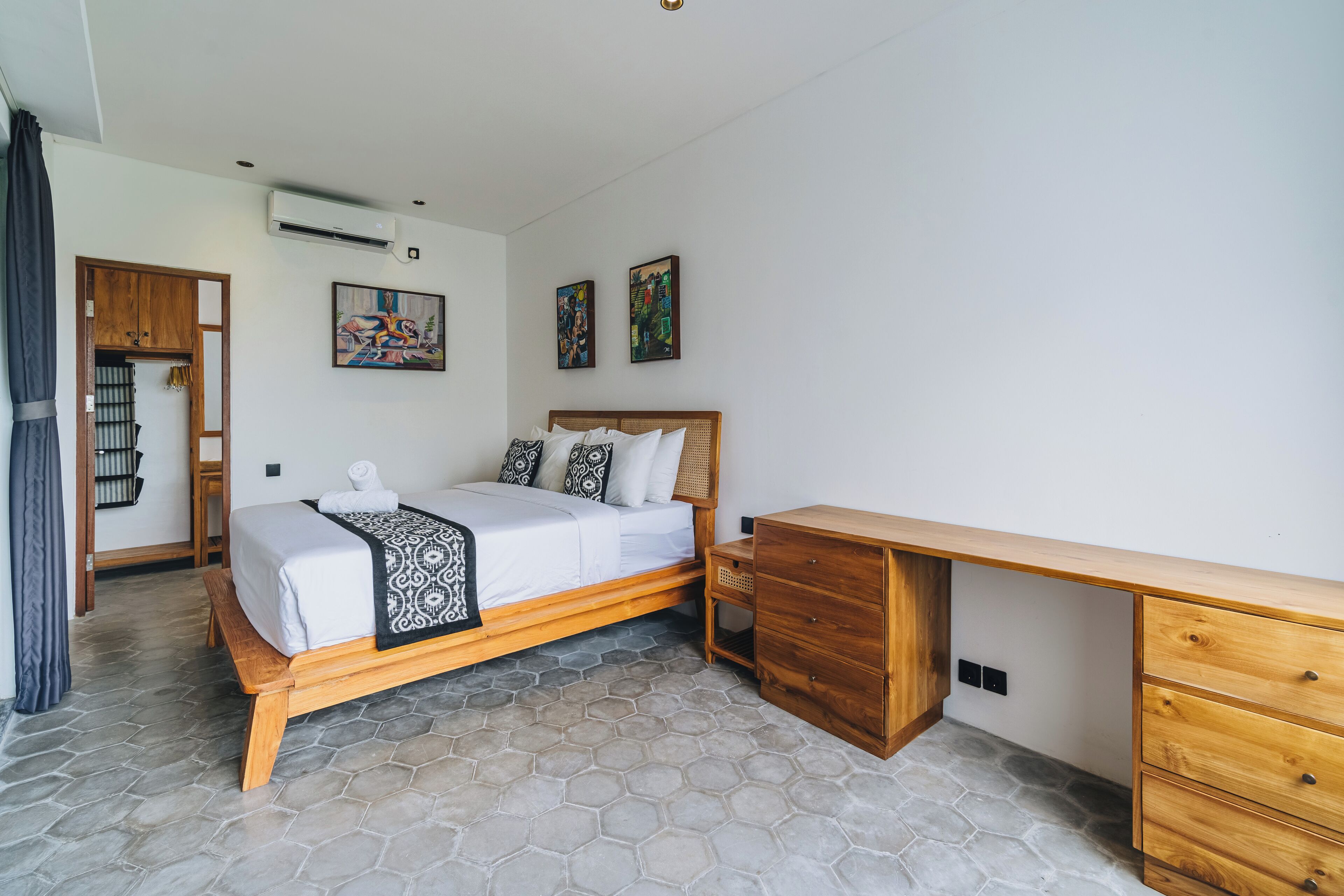 A bedroom with a bed, wooden desk, and artwork on the wall.
