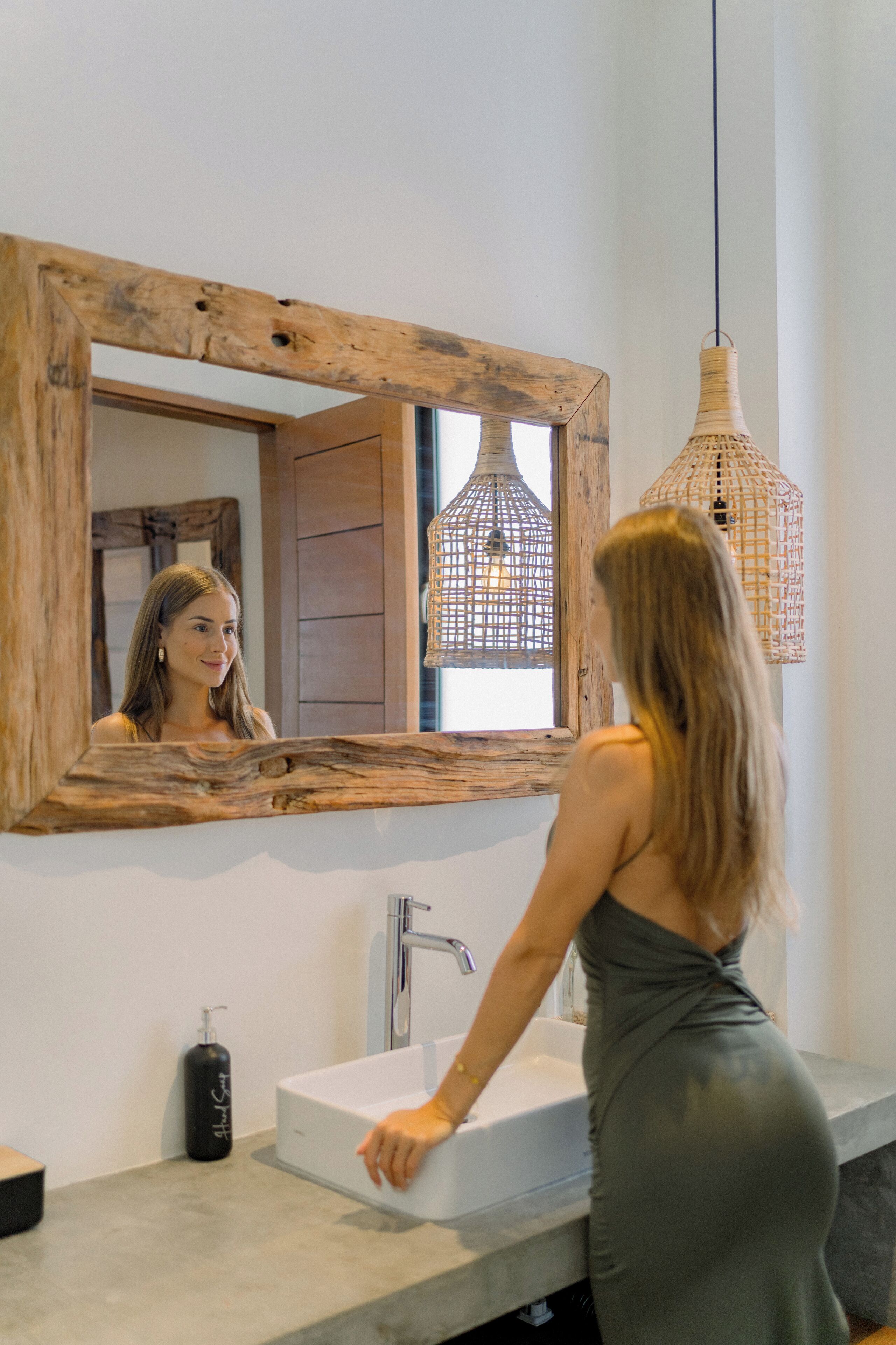 A bathroom with a wooden-framed mirror, a white sink, and a hanging light fixture.