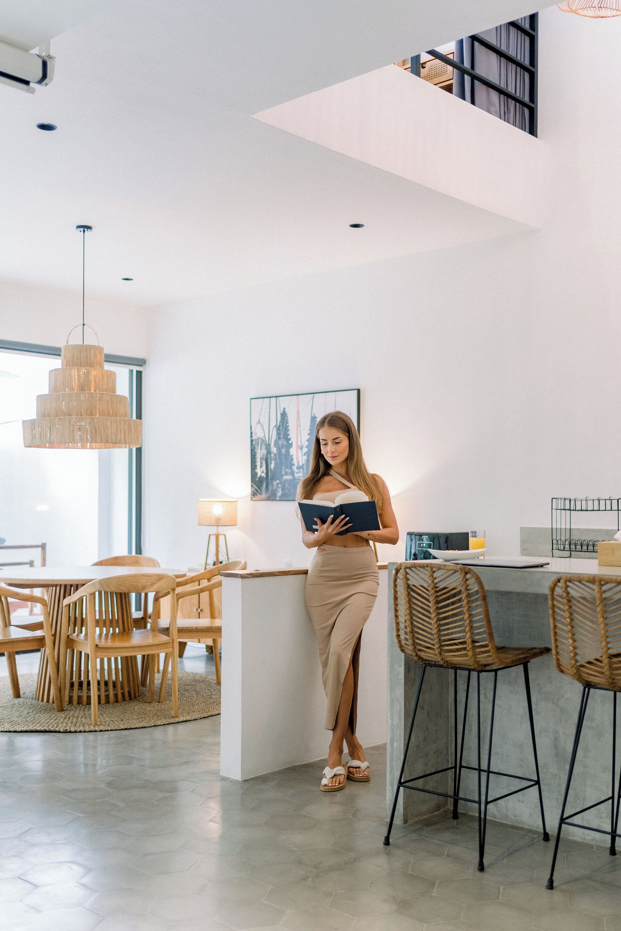A modern kitchen with a central island, wooden chairs, and a hanging light fixture.