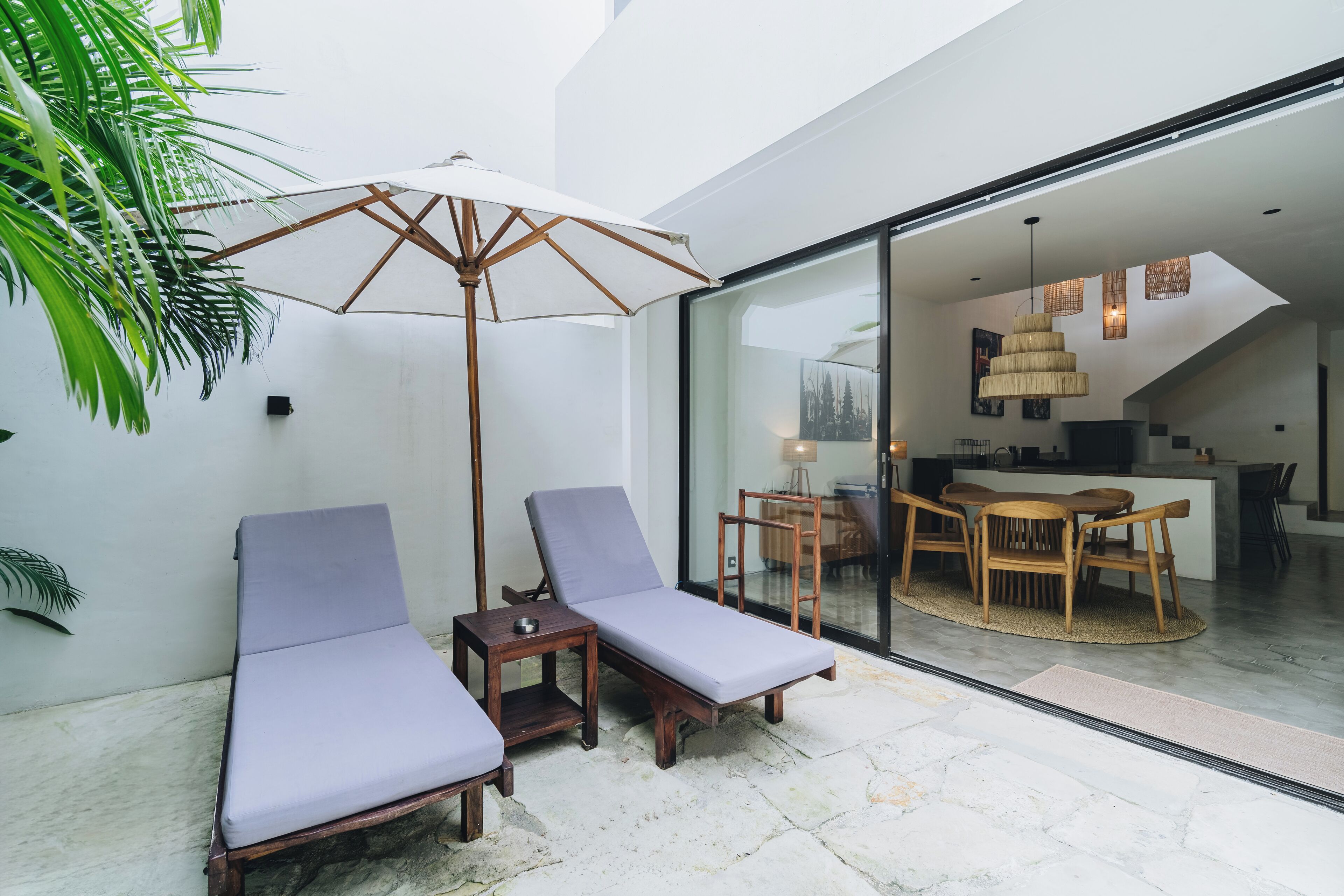 Un espacio lounge moderno al aire libre con dos sillones de madera, una mesita y un amplio parasol.