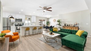 A modern kitchen with white cabinets, a microwave, and a dining area with a green sofa and yellow chairs. - Cozy Escape-Heated Pool-Perfect Location-SpringTRN (PHOENIX)