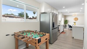 A modern kitchen with a foosball table, a stainless steel refrigerator, and a dining area with a small island. - Cozy Escape-Heated Pool-Perfect Location-SpringTRN (PHOENIX)