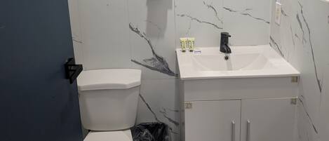 A bathroom with a toilet, sink, mirror, and marble walls.