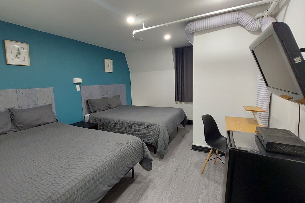 Habitación de hotel con dos camas, un escritorio con computadora, televisor y ventana con cortinas.