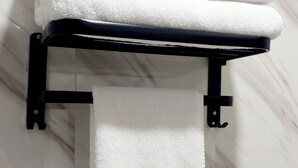 A black towel rack with three folded white towels and one hanging towel against a marble wall. - APD Hotel (Montreal)
