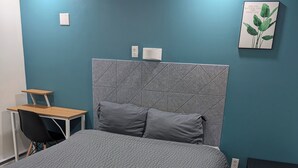 A bedroom with a bed, a desk, a chair, and a wall-mounted shelf. - APD Hotel (Montreal)