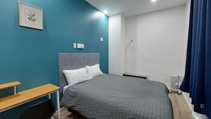 A bedroom with a bed, a bedside table, a wall-mounted light, and a radiator. - APD Hotel (Montreal)