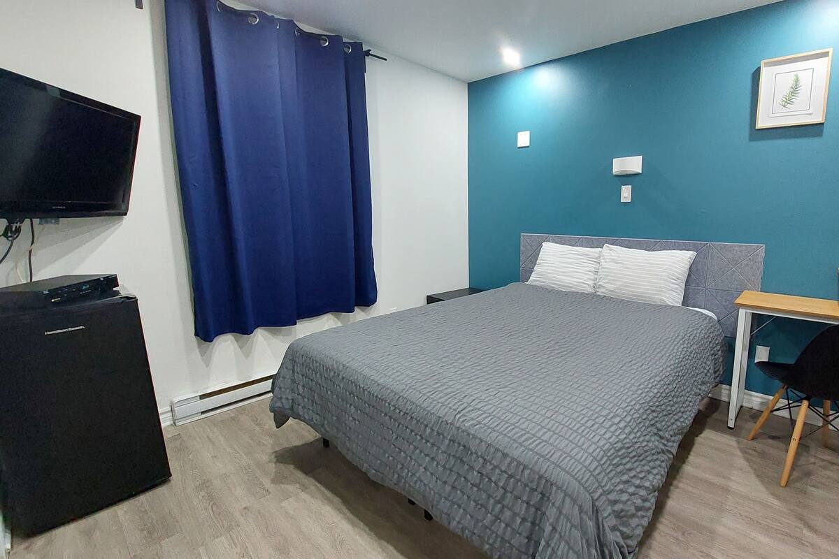 Un dormitorio con cama, escritorio, silla, televisión y cortina azul.