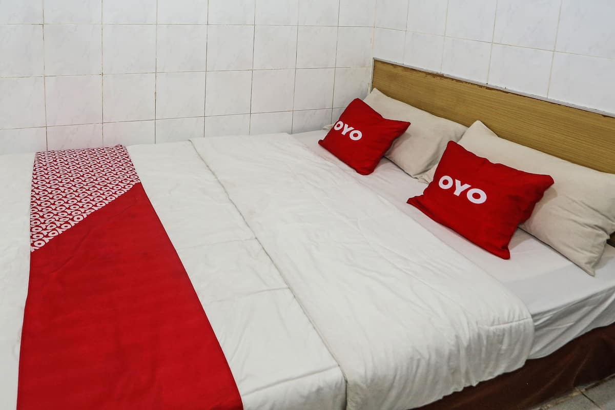 A bed with white bedding and two red pillows with the word "OYO" on them.