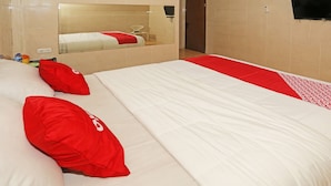 Ein Hotelzimmer mit einem großen Bett, rot-weiß gestreifter Bettwäsche, einem Spiegel und einem an der Wand befestigten Fernseher.