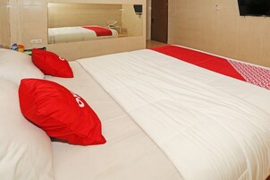 Ein Hotelzimmer mit einem großen Bett, rot-weiß gestreifter Bettwäsche, einem Spiegel und einem an der Wand befestigten Fernseher.