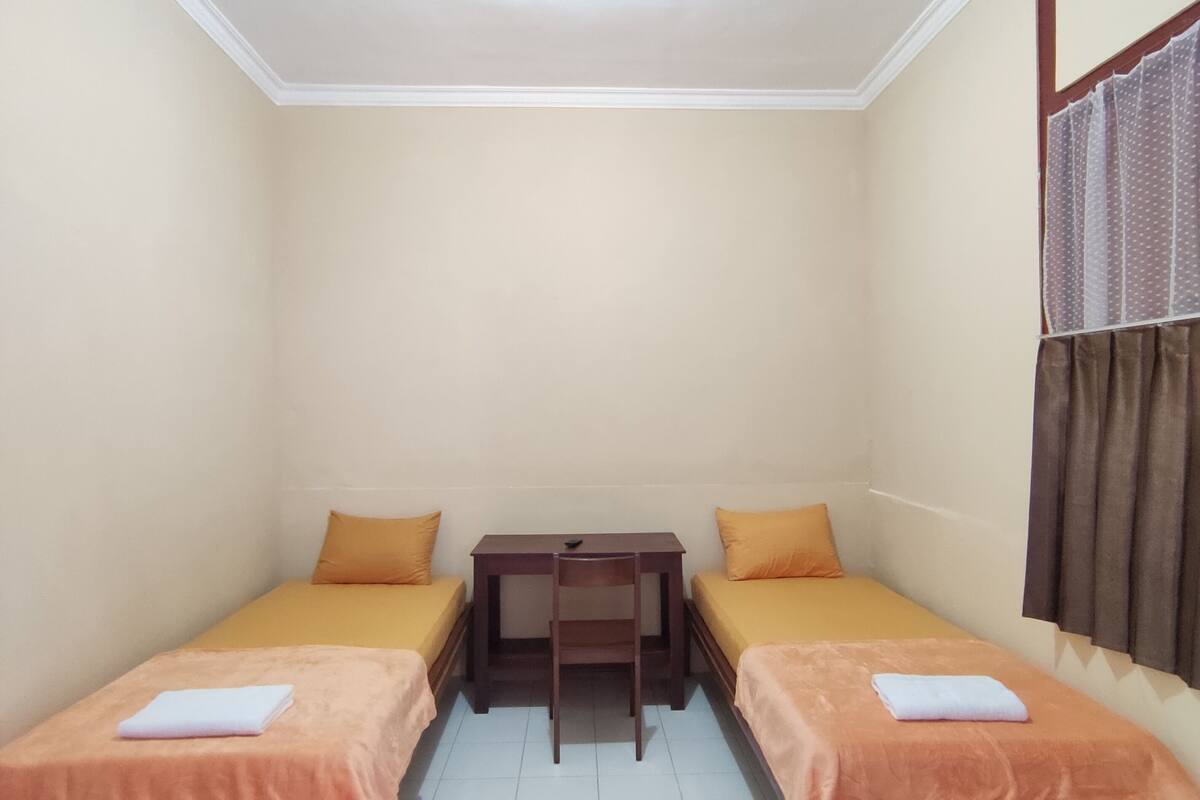 A small, clean room with two single beds, a small table, and a chair.