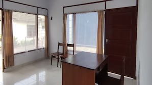 A room with a wooden desk, two chairs, a large window with curtains, and a door. - Hotel O Khazanah Room Syariah (Yogyakarta)