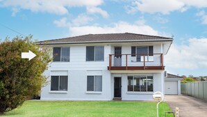 A two-story house with a balcony, a garage, and a well-maintained lawn. - Coastal Breeze (Ulladulla)