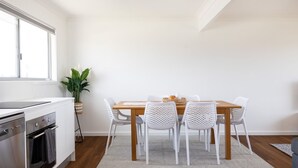 A modern kitchen with white cabinetry, a wooden dining table, and white woven chairs. - Coastal Breeze (Ulladulla)
