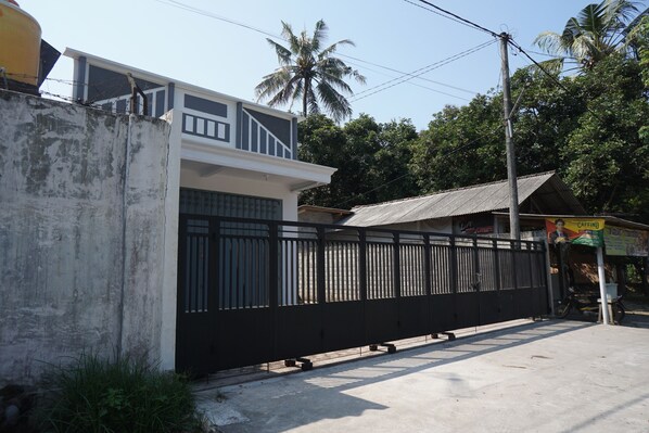 A gated residential area with a two-story house, a black metal fence, and a small shop with a signboard. - OYO Life 93185 Ayani Guest House (Blitar)