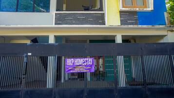 Un edificio con un letrero que indica 'HKP Homestay', que cuenta con un balcón y un ventanal con vista a árboles.