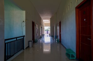 Um corredor comprido e estreito com portas em ambos os lados, bancos ao longo das paredes e uma lixeira no centro.