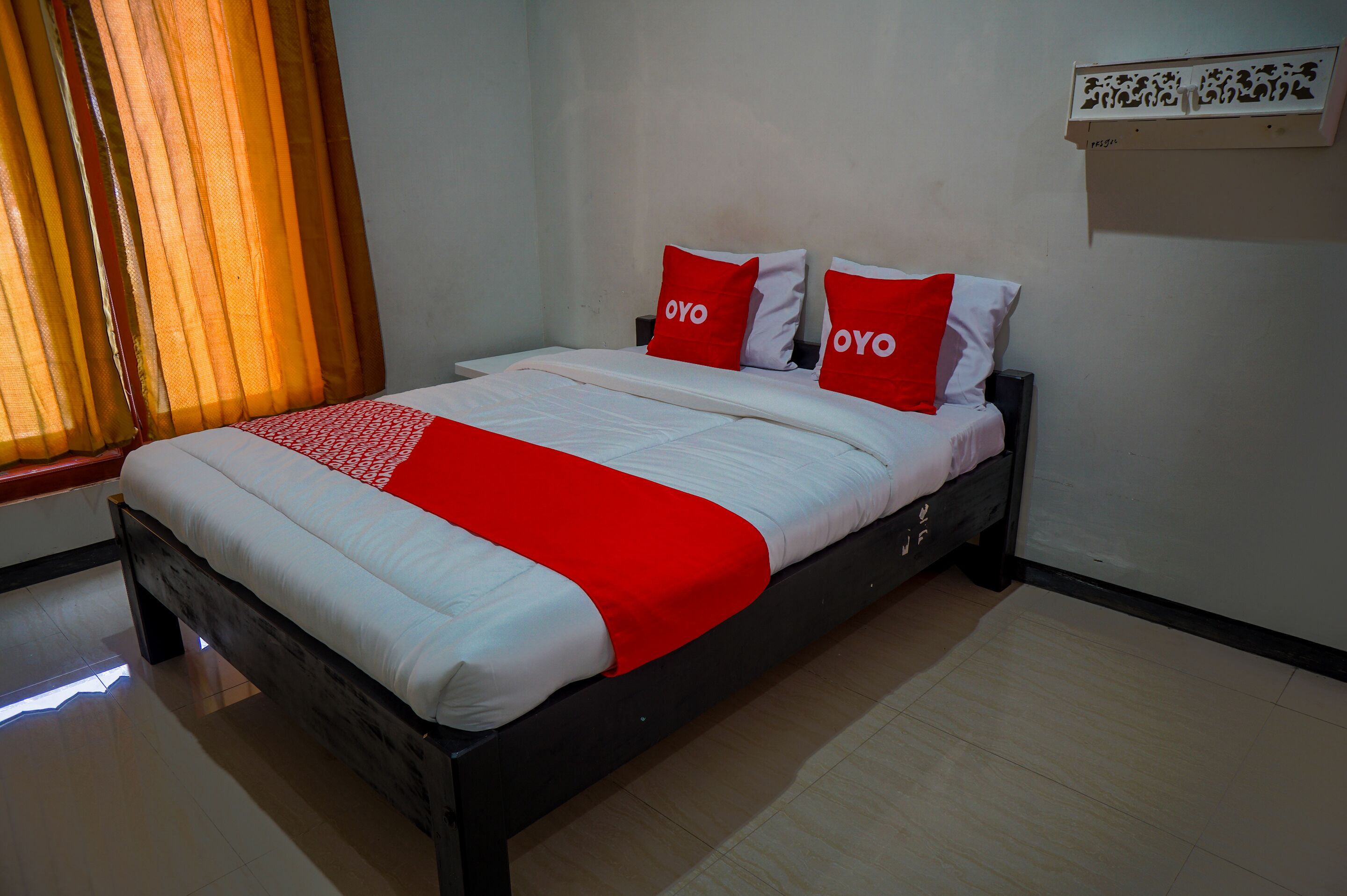 Una cama bien hecha con una colcha blanca y roja, dos almohadas con la palabra 'OYO' y un cabecero de madera.