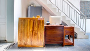 Un comptoir d’accueil avec un meuble en bois, un ventilateur et un panneau indiquant l’emplacement de la réception.