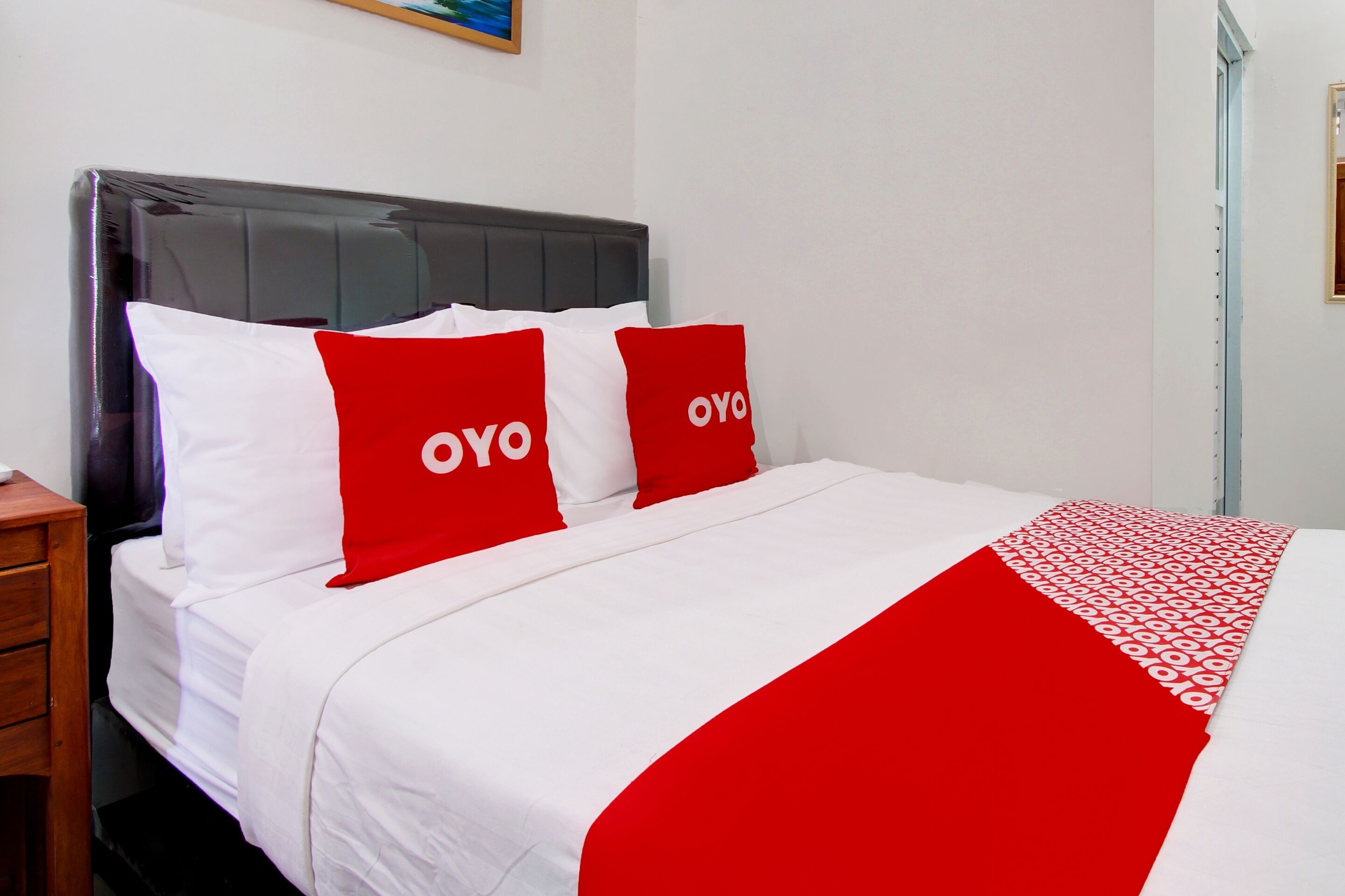 A hotel room with a bed, two pillows with the word "OYO" on them, a white bedspread, and a red and white patterned throw blanket.