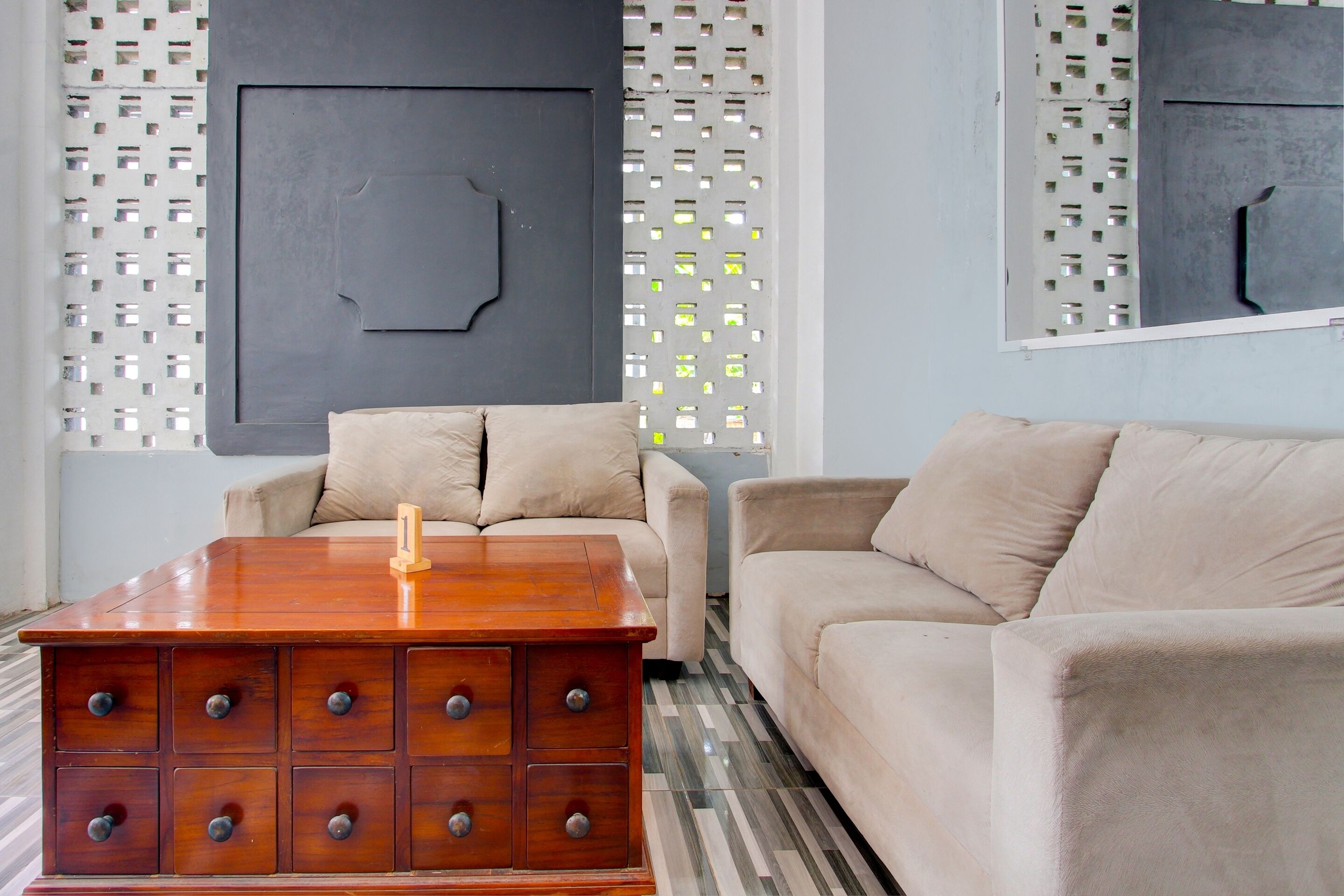 Un salon avec une commode en bois, des canapés de couleur beige et un mur orné d’un motif.