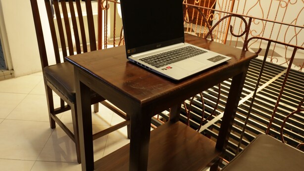 A laptop on a wooden table with a metal chair in the background. - SPOT ON 93189 Rumah Berkah Syariah (Blitar)