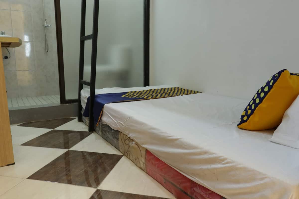 A hotel room with a checkered floor, a bed with a white mattress and a yellow pillow, and a wooden side table.