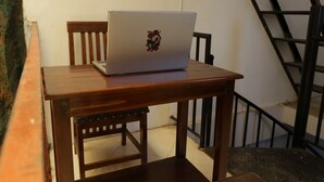 A laptop on a wooden table with a chair, a staircase in the background, and a wall with a textured surface. - SPOT ON 93189 Rumah Berkah Syariah (Blitar)