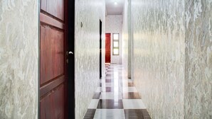 Un pasillo con paredes de mármol y piso a cuadros, que conduce a una habitación con puerta de madera y ventana.
