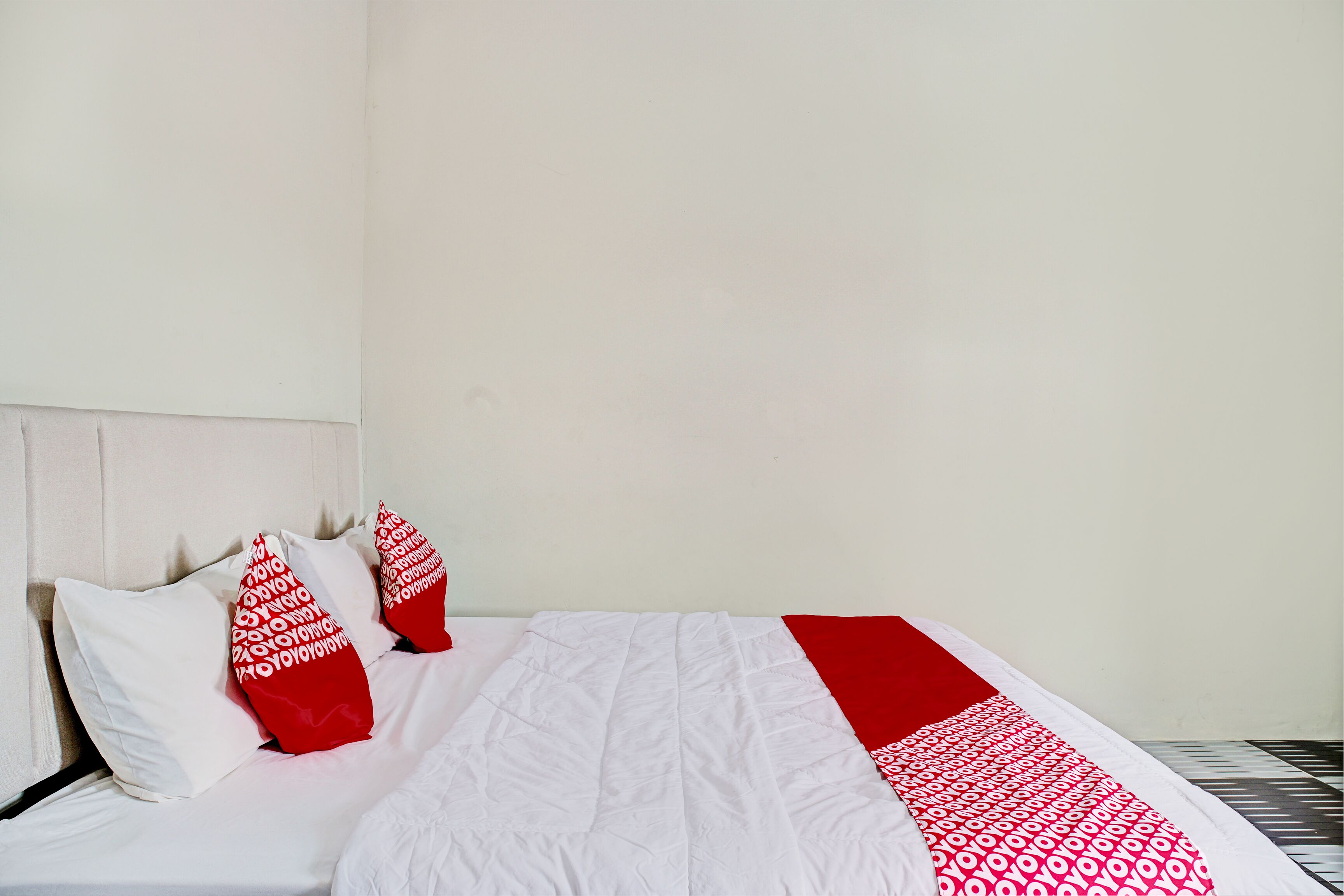 Een bed met witte lakens en rode kussens, een wit hoofdbord, en een deken met een rood-wit patroon.